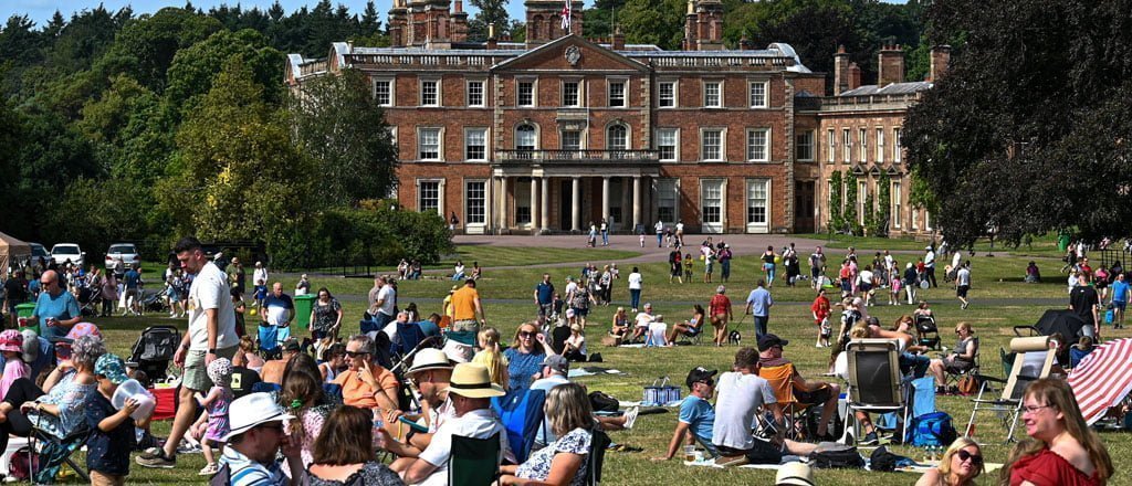 Large crowd of people enjoying the vibrant gardens at Weston Park in the summer. Colourful flowers and lush greenery surround visitors as they enjoy the park, soaking up the sun and engaging in various activities. Families, friends, and individuals relax on benches, picnic blankets, and the grass, chatting, laughing, and immersing themselves in the atmosphere of summer.
